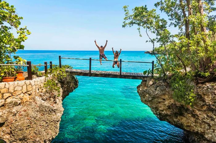 A man and woman leaping off a footbridge into the ocean at Negril, Jamaica