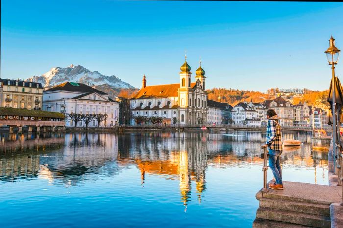 A man gazes at the Jesuit Church and Mount Pilatus from the banks of the Reuss River in Lucerne, Switzerland.