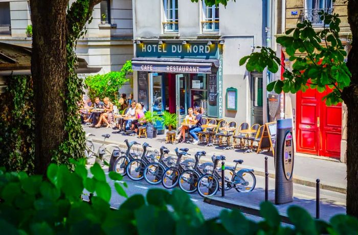 Diners enjoying food and drinks on the terrace of the renowned Hotel du Nord, with a bike-sharing station in the foreground