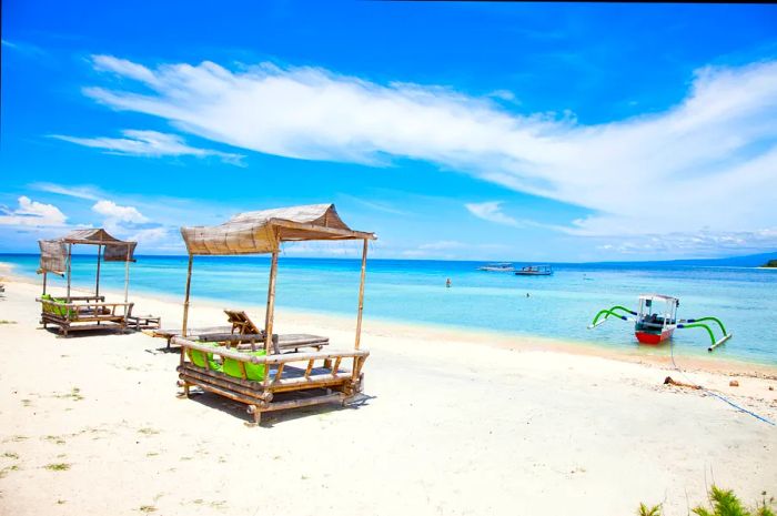 Two palm-thatched beach huts on a pristine white sand beach beside a turquoise sea