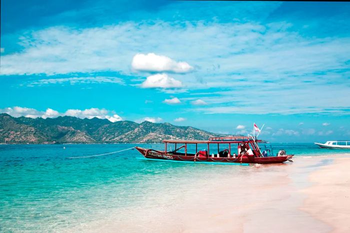 A red dive boat rests on the beach, with canisters neatly lined up alongside it.