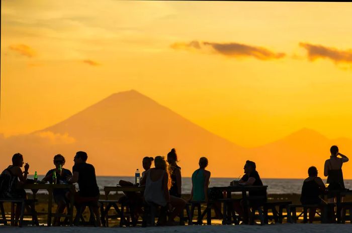 Silhouetted figures watch the sunset as it casts a glow over the island of Bali, with the iconic Gunung Agung volcano dominating the landscape