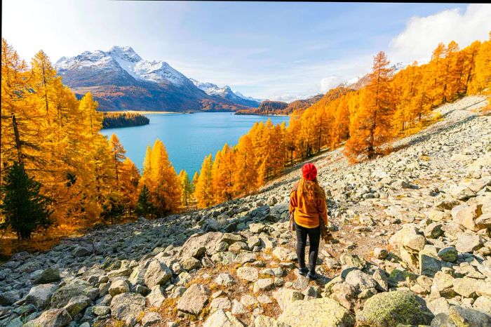 A woman gazes at La Margna Peak and Lake Sils during autumn in Sils Im Engadin, Maloja region, Canton of Grisons, Switzerland.