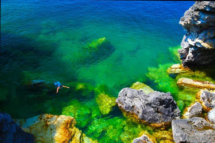 A swimmer in turquoise waters near a rocky shoreline