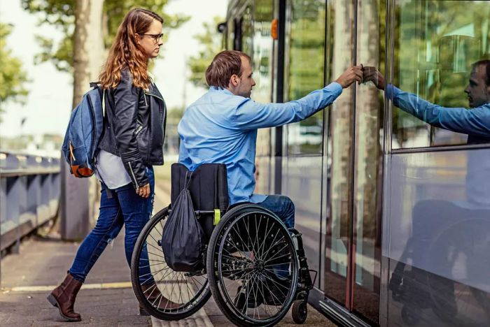 A man in a wheelchair boarding a tram with his girlfriend in the Netherlands.