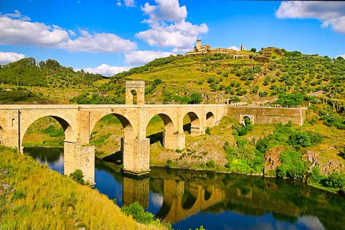 A historic bridge spans a river in Extremadura, Spain.