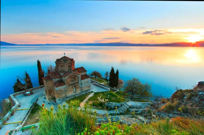 A quaint stone church perched by a lake at sunset