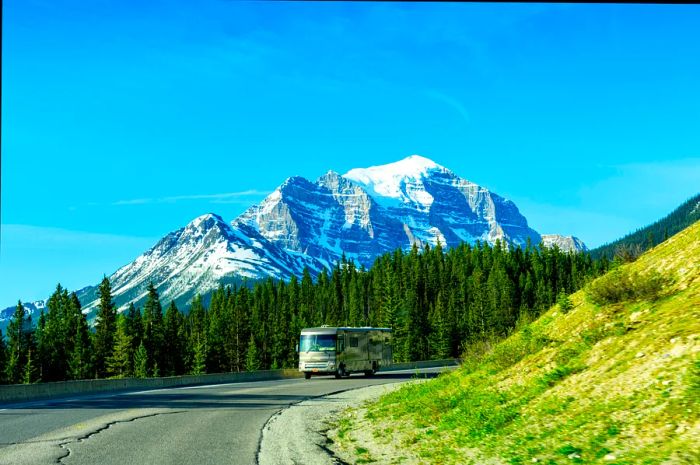 A spacious motorhome navigates a curve along a road winding through a forested mountain scene.