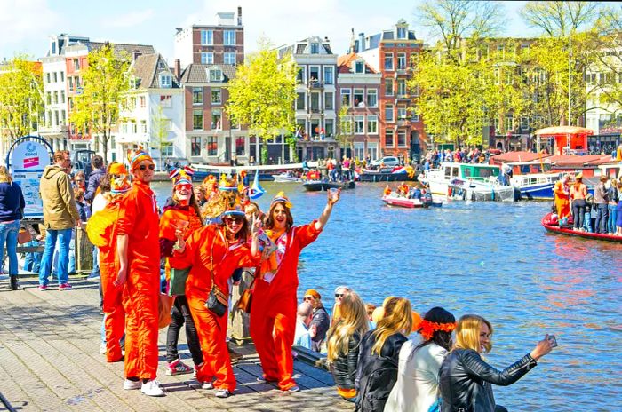 People in orange celebrate by a canal in a city