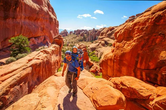 A hiker carrying a baby in a backpack enjoys the adventures of Arches National Park.