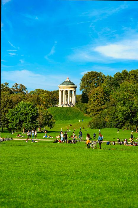 People relax on the grass near a small, round temple-like structure perched atop a hill.