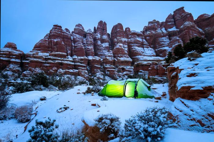 A snow-covered tent illuminated after dark in the Utah desert.