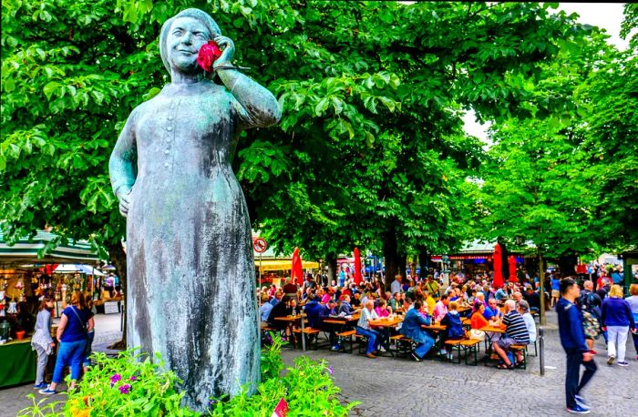 A statue rises amid greenery, while tables are filled with diners enjoying fare from nearby market stalls