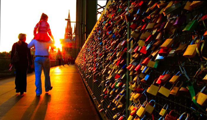 Visitors stroll past numerous padlocks attached to railings on a bridge