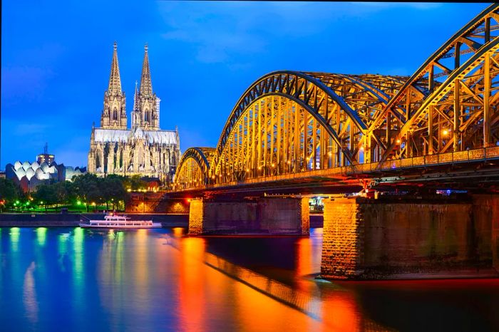 A stunning view of a grand cathedral illuminated at night beside a river with a bridge crossing over.