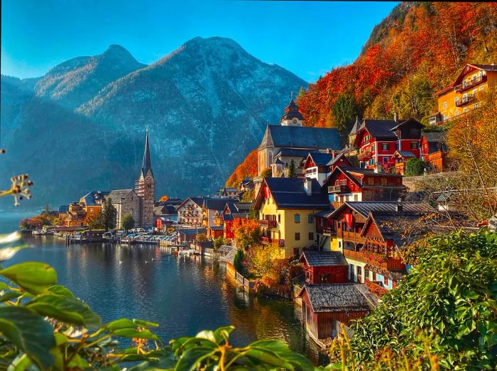 Historic Hallstatt perches on the shores of a serene, reflective lake, framed by majestic mountains. The foliage transforms into brilliant shades of orange and red.