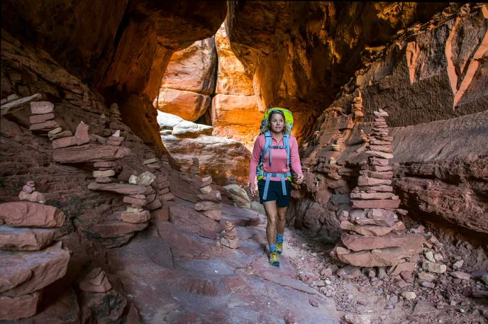 A woman backpacking past stone cairns along the Joint Trail in the Needles District of Canyonlands National Park, Monticello, Utah