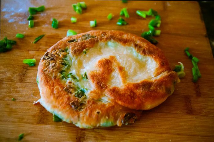 A green onion cake displayed on a wooden chopping board with sliced scallions around it.