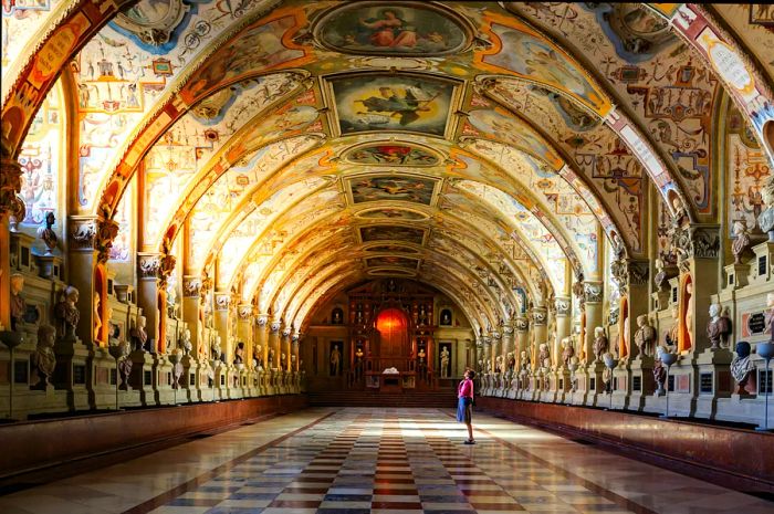 A woman gazes at the intricately adorned, arched ceiling of a room.