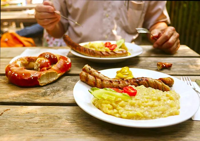 A large pretzel, grilled sausages, and potato salad served in a Bavarian beer garden