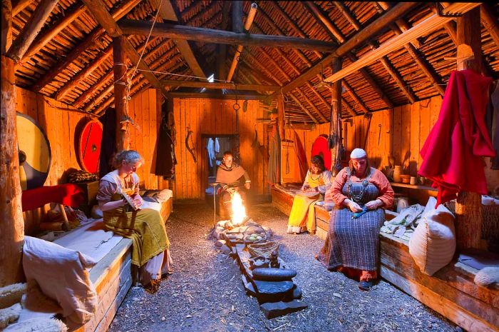 Parks Canada interpreters in historical costumes performing traditional tasks inside a reconstructed Viking longhouse at L’Anse aux Meadows National Historic Site, Newfoundland, Canada