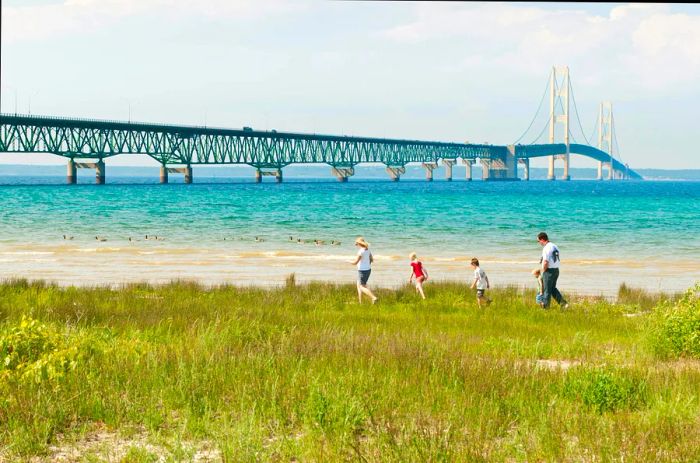 A family strolls along the grassy banks of a waterway with a grand bridge in the background