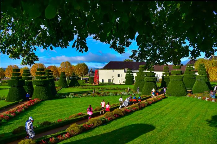 Costumed participants dash along a path through beautifully landscaped gardens, with a grand manor house in the backdrop