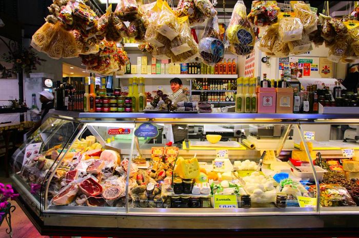 A vendor showcases a variety of cold meats, cheeses, and dry goods at a stall in Florence's Mercato Centrale.