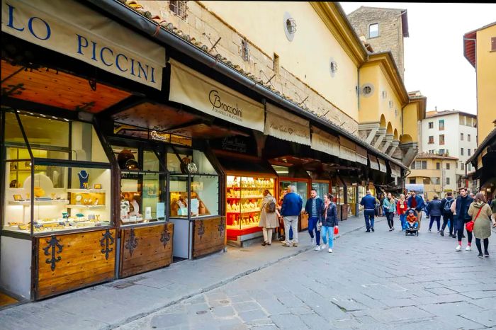 Shoppers meandering along the Ponte Vecchio, a medieval bridge lined with shops featuring luxury items like jewelry