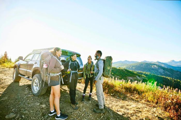 A cheerful father stands beside his three daughters at the back of their car, ready for a hiking adventure in Washington State.