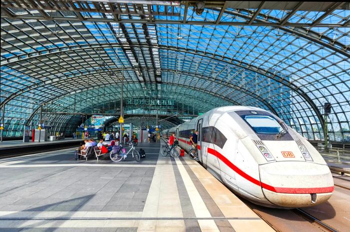 Passengers, some with bikes, board a high-speed train at a spacious station featuring a glass roof