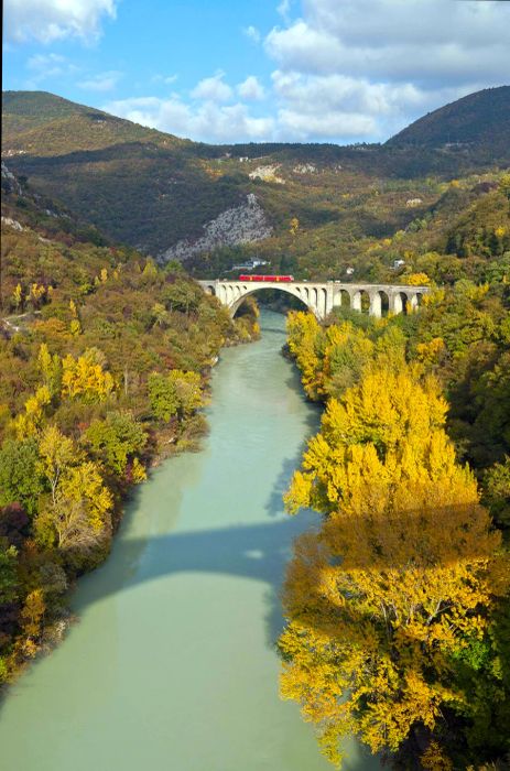 A train travels over a stone bridge spanning a swiftly flowing river