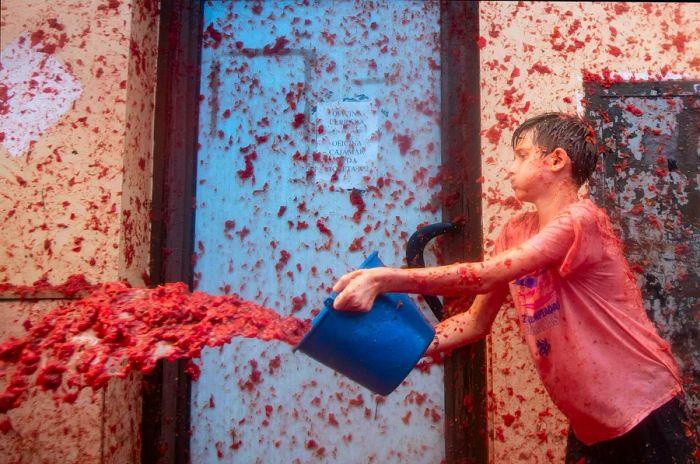 A boy uses a bucket to hurl smashed tomatoes during the La Tomatina tomato-throwing festival in Buñol, Spain