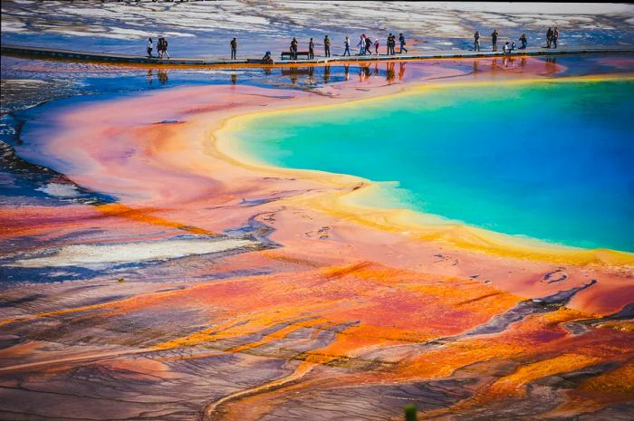 Visitors stroll along a boardwalk by a bright turquoise lake