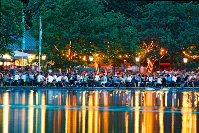 People enjoy outdoor seating at the Seehaus beer garden, with their reflections in the water