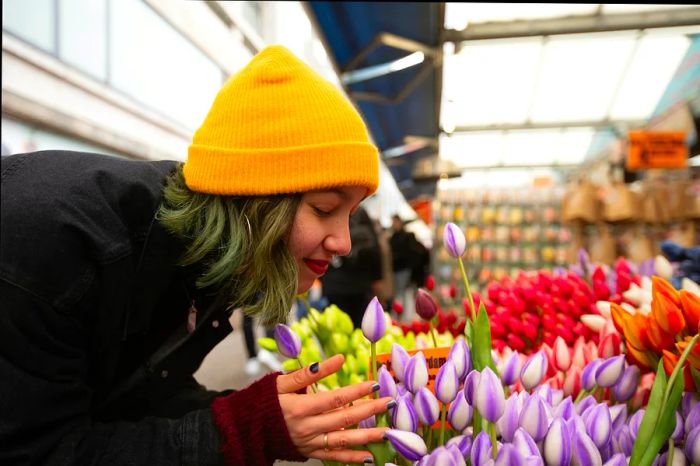 A woman in a yellow hat leans in to enjoy the fragrance of a bouquet of tulips.