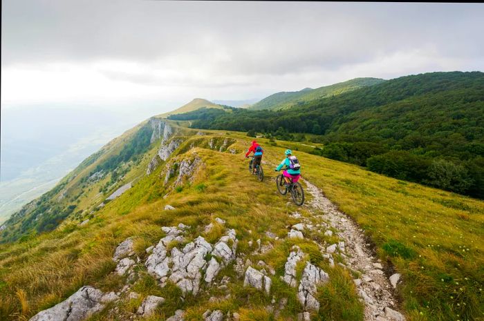 Two cyclists on a cliffside biking trail