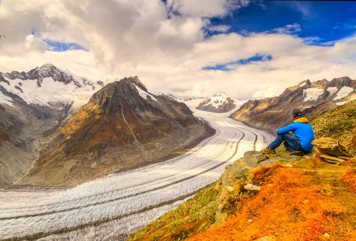 A hiker pauses to admire the majestic Aletsch Glacier as it weaves through the mountains of the Alps.