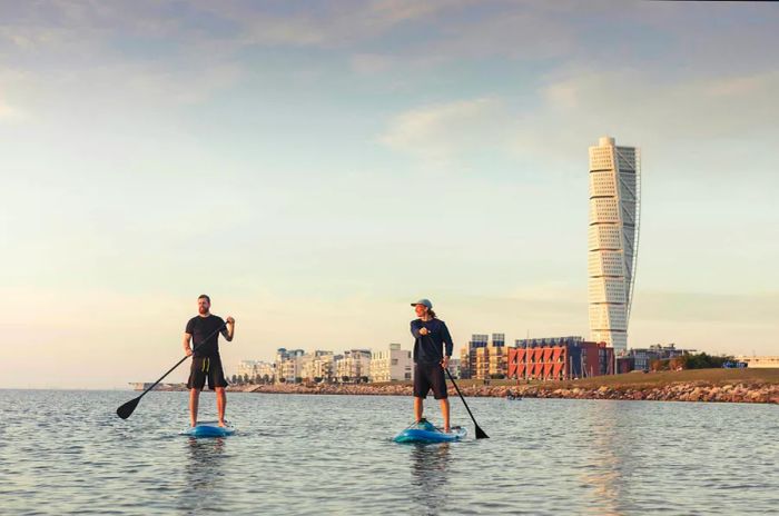 Two friends paddle boarding in front of the Turning Torso tower.