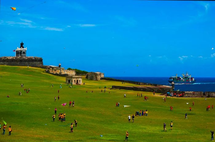 Children and parents are flying kites in front of a historic seaside fortress