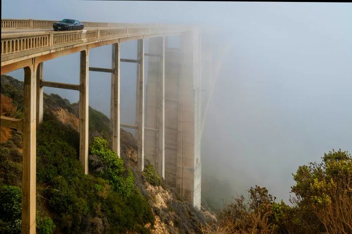 A vehicle crosses the iconic Bixby Bridge enveloped in fog, Big Sur, California, USA