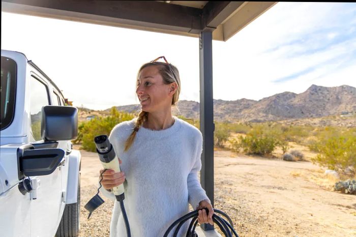 A woman connects her electric vehicle to a charging station in a desert setting, Western USA