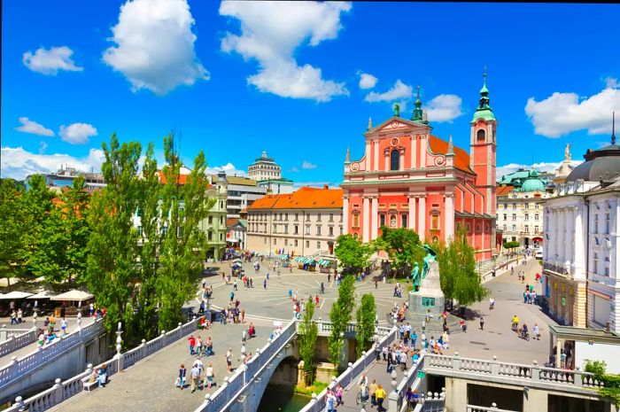 A striking red building stands out in a city square adjacent to a river.