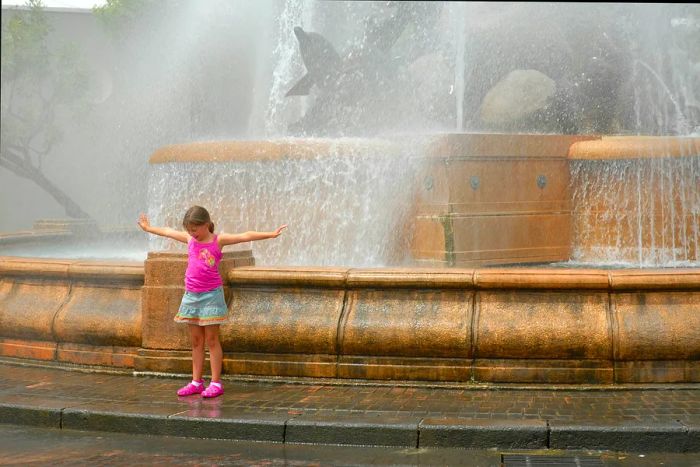 A young girl enjoying the refreshing mist from a fountain