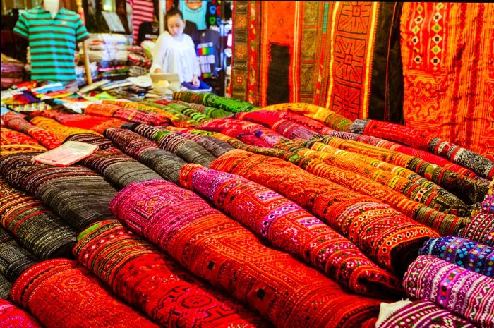 A night market stall in Chiang Mai, Thailand, displays a vibrant array of woven textiles for sale