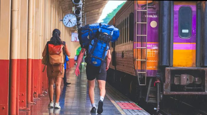 A man and woman with backpacks make their way to a train waiting at the platform in Chiang Mai station.