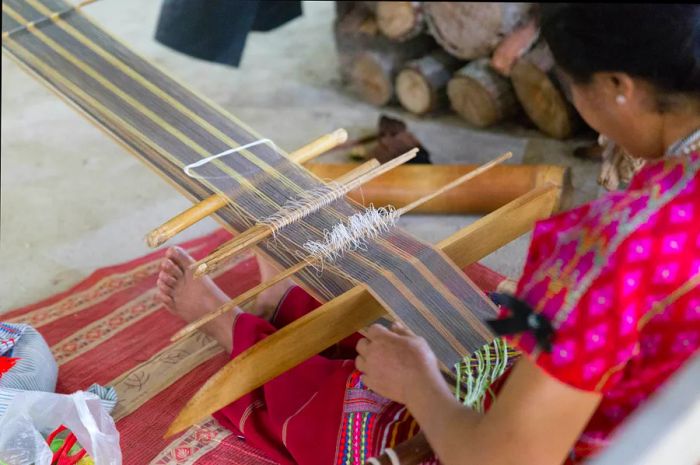 A woman weaves fabric using a traditional loom, showcasing local craftsmanship.