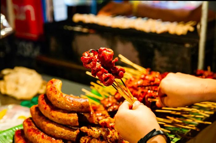 Hands holding meat skewers at a street stall in Chiang Mai, Thailand