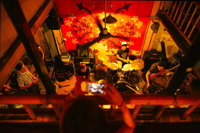 A concert-goer stands on a balcony, capturing a photo of the band performing below at North Gate Jazz Co-Op in Chiang Mai.