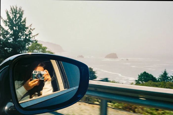 A woman captures a mirror selfie showcasing the coast while driving along a scenic road in Seaside, Oregon, USA